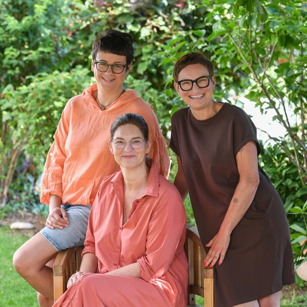 Das Leitungs-Team der Krümelkiste: drei Frauen von jünger bis mittleren Alters läscheln oder lachen. Alle drei tragen eine Brille. Foto aus dem Garten der Krümelkiste.