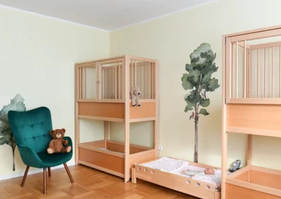 Helles Zimmer mit Stockbetten aus Holz, die Wände sind mit Bäumen bemalt, in den Betten liegen Kuscheltiere.