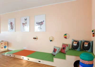 Anderer Teil des Teil des Spielzimmers mit verschiedenen Spiel-Möbeln, bunten Kissen und Wand-Spielzeug.